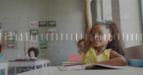 Elementary student raising right hand at desk while learning in bright modern classroom