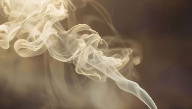 Translucent curling smoke ribbons creating soft abstract wisps over warm brown background