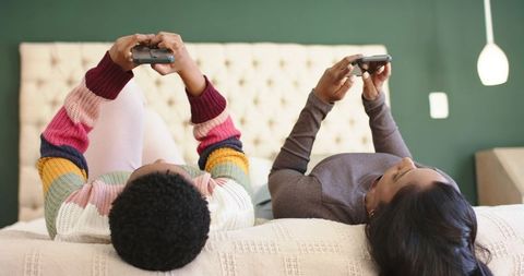 Diverse Friends Gaming with Controllers on Comfortable Bed