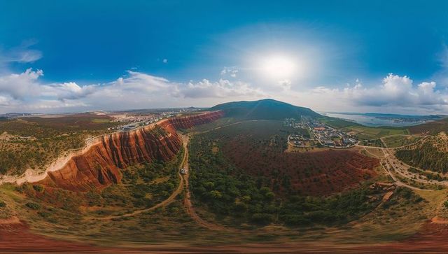 Red sandstone cliff ridge descending into coastal valley with winding dirt track, panoramic