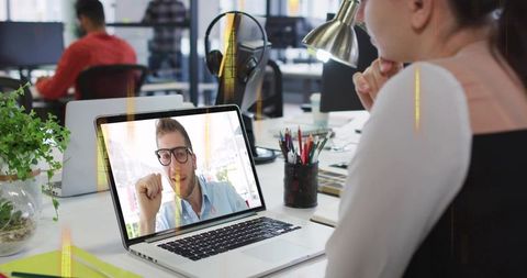Remote team meeting in modern open office with woman video calling on laptop