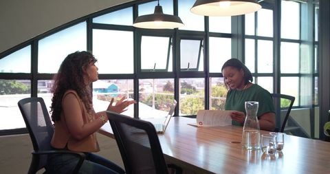 Women collaborating in bright modern office meeting room with laptop and documents