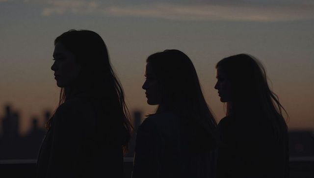 Three women silhouettes standing on rooftop overlooking city skyline at dusk moody backlit
