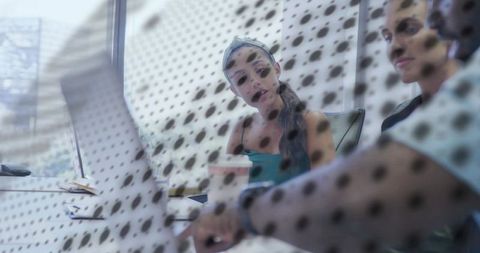 Female colleagues collaborating over laptop behind perforated glass in modern office