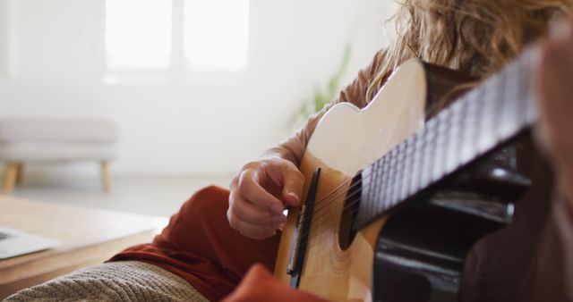 Midsection of caucasian woman playing acoustic guitar, sitting in sunny cottage living room - Download Free Stock Photos Pikwizard.com