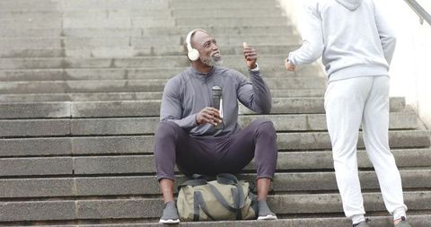 Senior african american man resting on urban steps after workout, listening with headphones