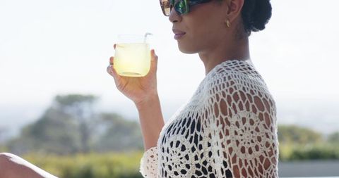 African american woman relaxing on terrace sipping lemonade in white crochet coverup