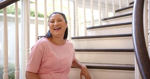 Smiling Woman Relaxing on Home Staircase in Cozy Pink Attire