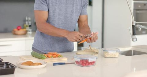 African american man peeling carrot on modern kitchen island for healthy meal prep at home