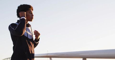 Athletic Runner Preparing with Earbuds on Pedestrian Bridge at Dawn