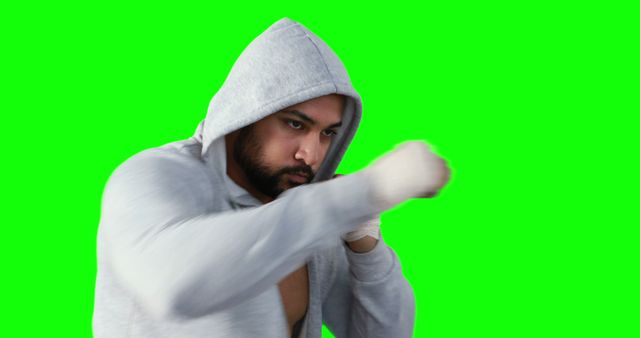 This image shows a man in a grey hoodie throwing a punch against a green screen. Excellent for fitness, exercise, and sports-related content, as well as martial arts promotions and training tutorials. The green screen allows for easy background replacement in various editing projects.