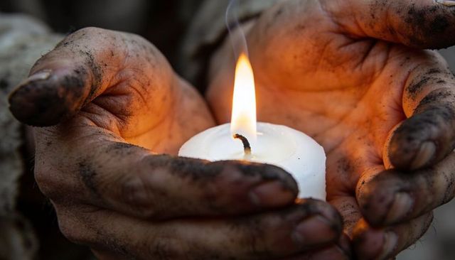 Grimy hands holding lit candle, closeup of melted wax and sooted palms