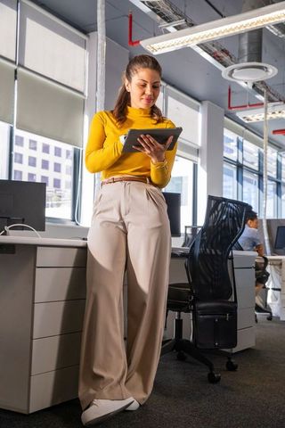 Confident asian woman leaning on desk using tablet in modern open-plan office for teamwork