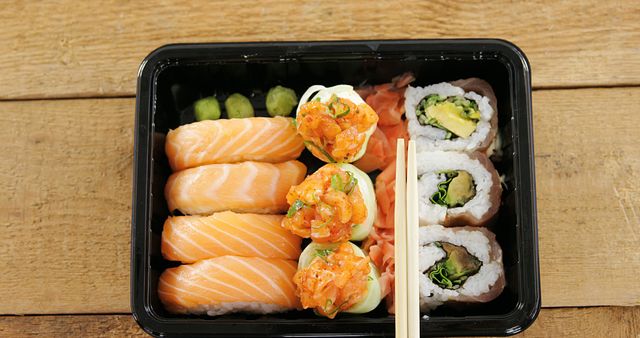 Sushi rolls with salmon in plastic tray on wooden background