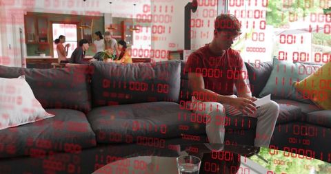 Young man reading documents on couch with red binary overlay conveying data breach anxiety