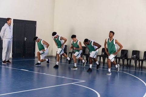 Basketball team practicing lunges on indoor court with coach