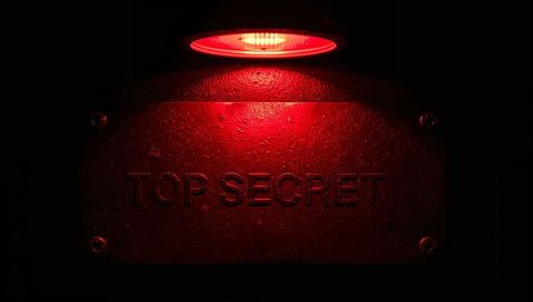 Glowing red spotlight illuminating embossed top secret metal plaque on secured door