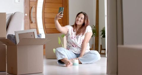 Smiling Woman Taking Selfie in New Home Surrounded by Moving Boxes