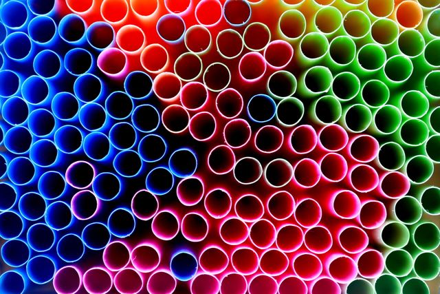 Vividly colored plastic straws seen from above, forming a repetitive circular pattern. Each straw reflects a different color, creating a rainbow effect. Perfect for use in background designs, abstract art projects, or advertisements focusing on sustainability and environmental matters.