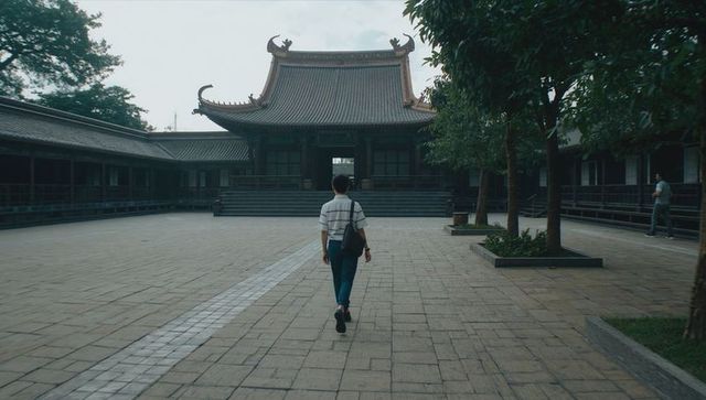 Traveler walking through temple courtyard toward ornate pavilion with heritage rooflines