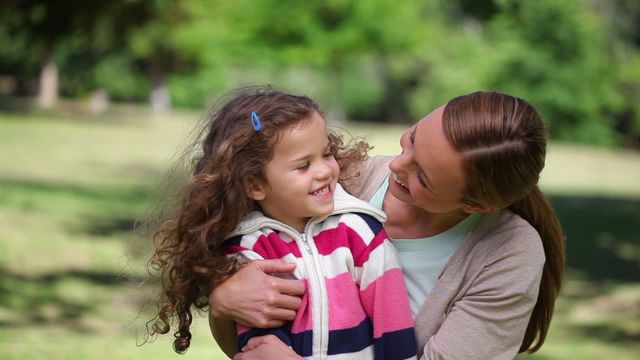 Mother joyfully hugs her daughter in a sunny park. Perfect for advertising family values, emotional connections, parental love, and outdoor leisure activities. Ideal for websites, brochures, or campaigns highlighting family life or promoting kids’ clothing and outdoor products.