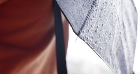 African American man holding wet umbrella and wearing brown coat on rainy city street