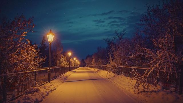 Vintage street lamps illuminate snowy park path at night