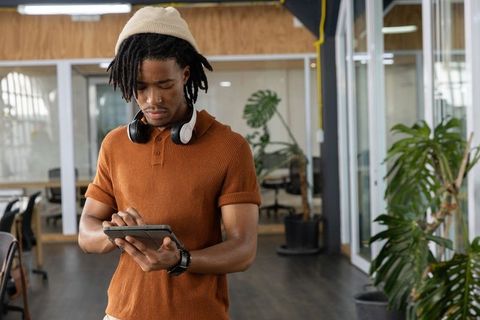 African American man using tablet in modern coworking space with headphones and plants