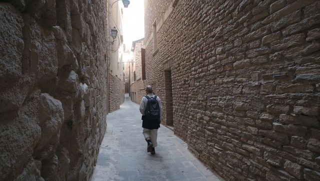 Solitary Traveler Walking Narrow Stone Alleyway Between Historic Masonry Walls with Lanterns