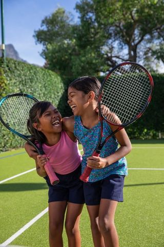 Sisters laughing and embracing with tennis rackets on court