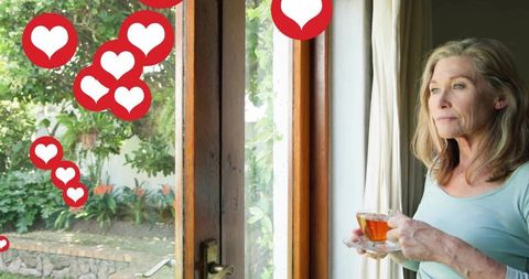 Mature woman holding teacup gazing through wooden door to garden with heart overlays