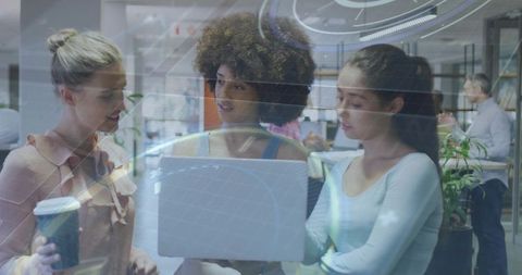 Multicultural team collaborating over laptop with holographic interface in modern open-plan office
