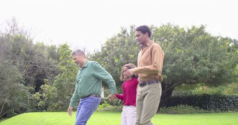 Family walking hand-in-hand on lush park lawn under overcast sky wearing casual button-ups