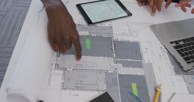 Hands of biracial male and female architects using tablet and checking architects plans in office. creative business and office workplace.