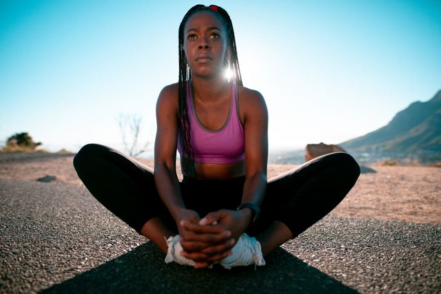 This image shows a fit African American woman stretching outdoors at sunset, embodying a healthy and active lifestyle. Ideal for use in fitness blogs, wellness websites, outdoor activity promotions, and health-related advertisements.