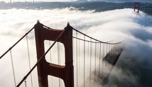 Golden gate bridge tower piercing dense san francisco fog, aerial suspension panorama