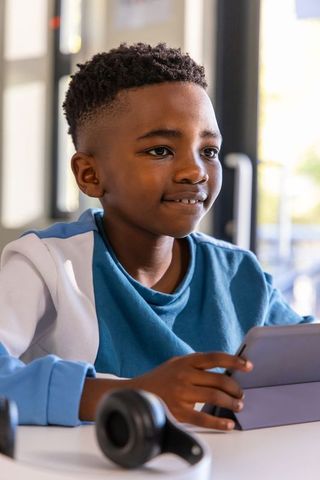 African american schoolboy using tablet and smiling while learning in bright classroom