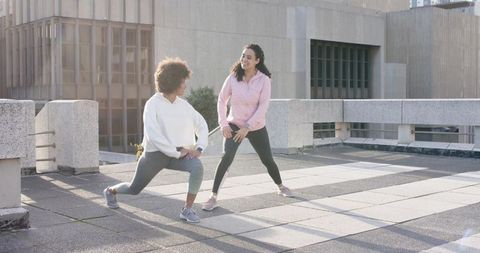 Two Women Stretching on Urban Rooftop at Sunrise for Friendly Outdoor Workout