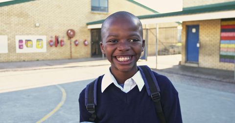 Smiling schoolboy outdoors with backpack in schoolyard