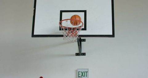 Basketball Swishing Through Hoop Above Exit Sign in Gym