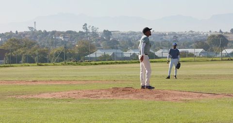 African American Pitcher Standing on Mound with Teammate in Outfield, Suburban Baseball Scene