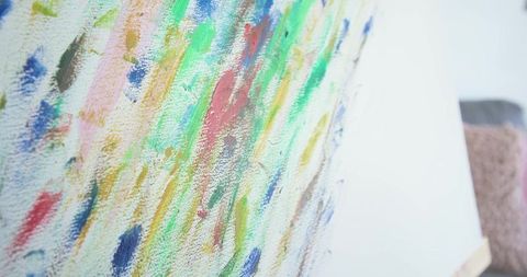 Vibrant impasto brushstrokes on textured canvas leaning against white studio wall closeup