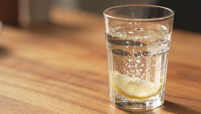 Refreshing sparkling water with lemon wedge in tall glass on wooden table, minimalist