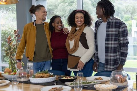 Multiracial friends laughing and sharing roasted dinner around cozy dining table