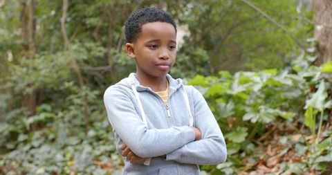 African American boy standing with folded arms in contemplative forest wearing hoodie