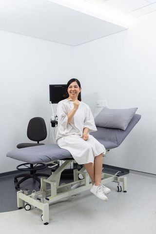 Smiling patient sitting on exam table in modern clinic wearing gown and sneakers