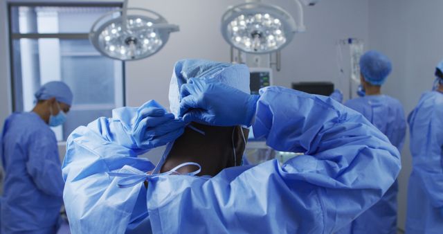 African american male surgeon putting on protective clothes standing in operating theatre. medicine, health and healthcare services.
