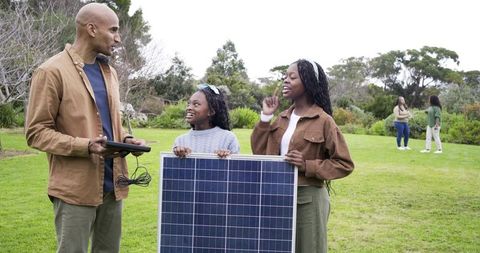 Mature man demonstrating solar panel to african american girl and teenager in park outdoors