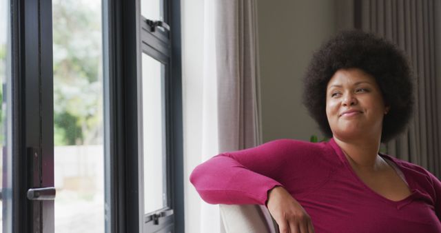 Image of happy plus size african american woman looking outside window. lifestyle, leisure, spending free time at home.