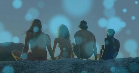 Friends Enjoying Ocean View on Rocky Ledge at Sunset